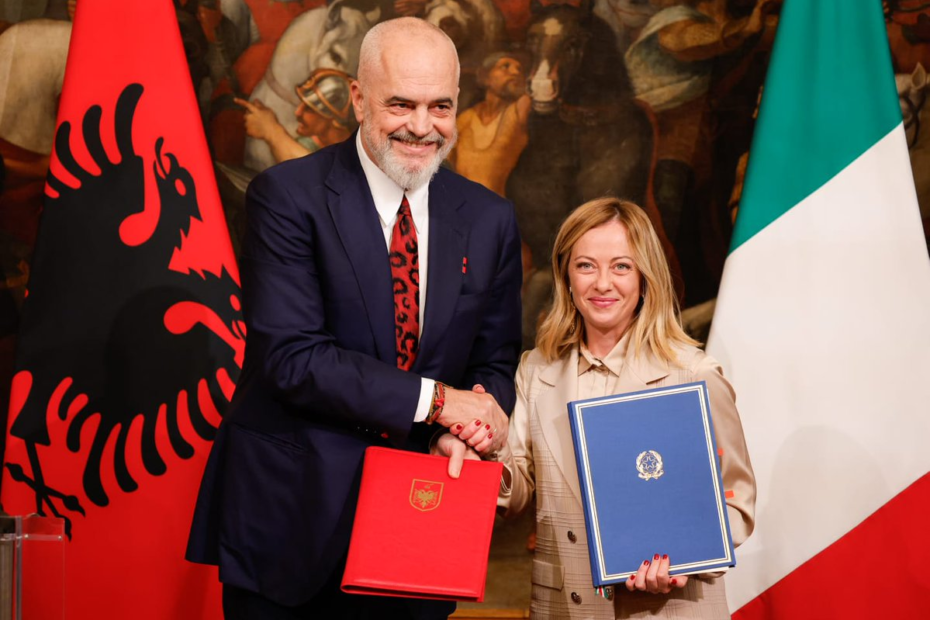 Italian Prime Minister Meloni and Albanian Prime Minister Edi Rama shake hands with the countries' flags behind them.