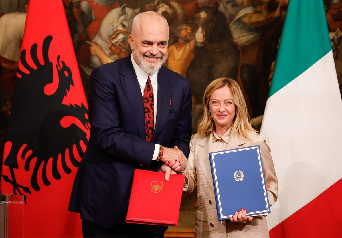 Italian Prime Minister Meloni and Albanian Prime Minister Edi Rama shake hands with the countries' flags behind them.